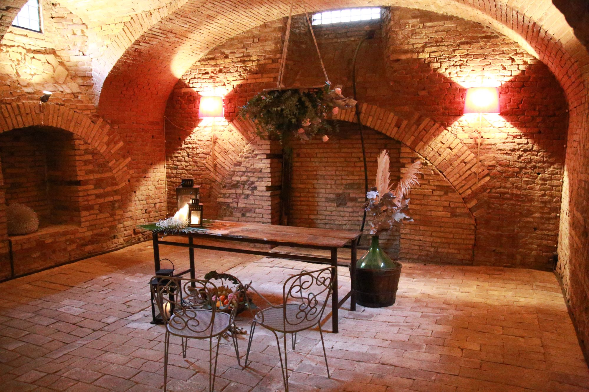Tavolo in legno con lanterne e fiori sotto le volte in mattoni della Cantina