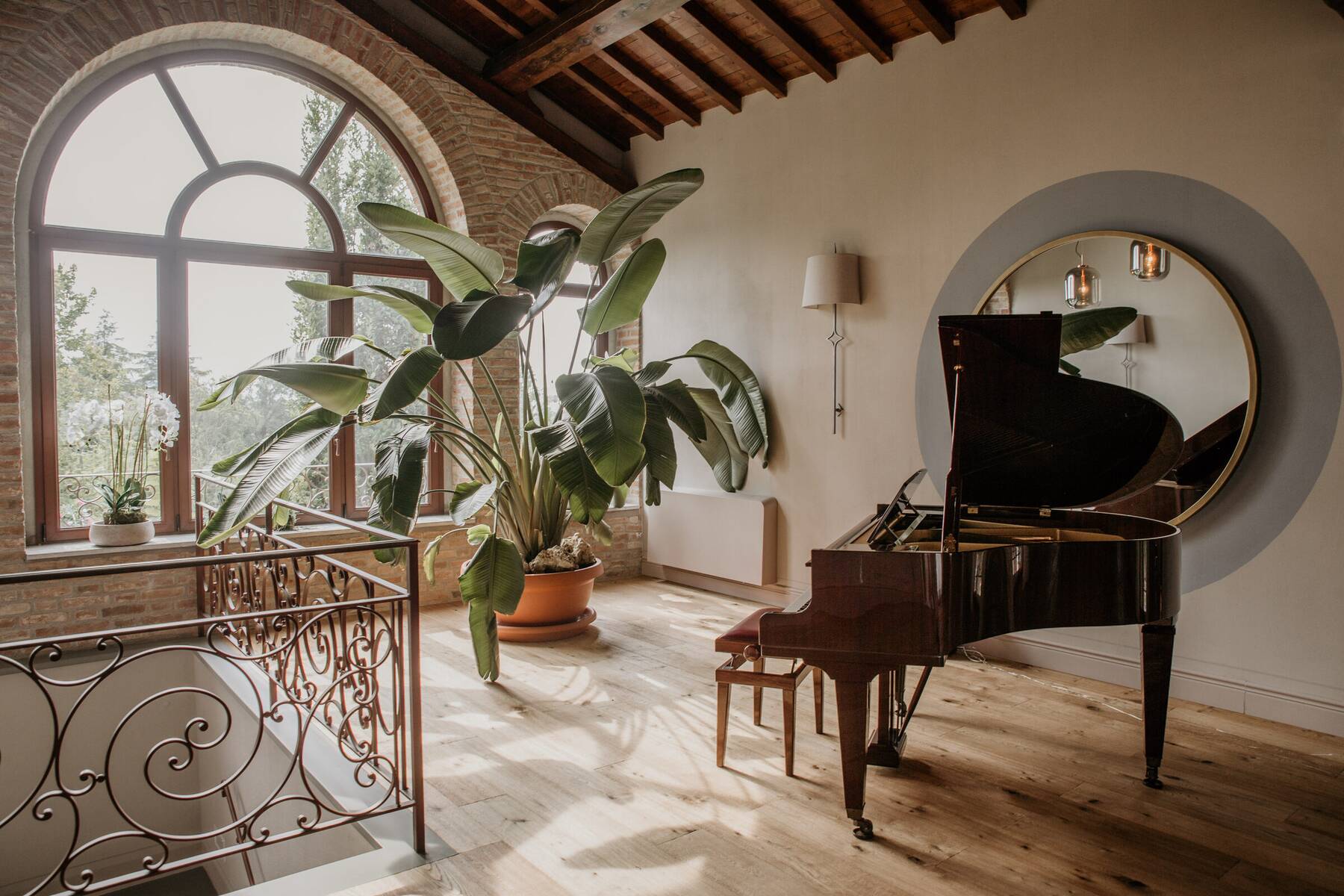 Il pianoforte a coda vicino al finestrone ad arco, con lo specchio rotondo e la scala in ferro battuto