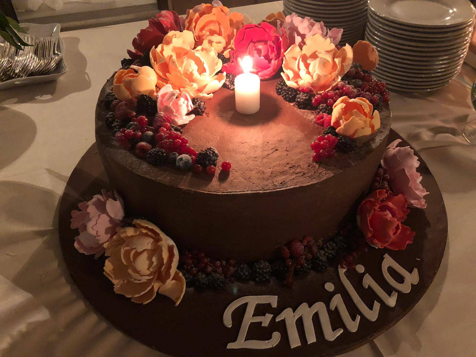 Torta di compleanno decorata con fiori e frutti di bosco, candela accesa