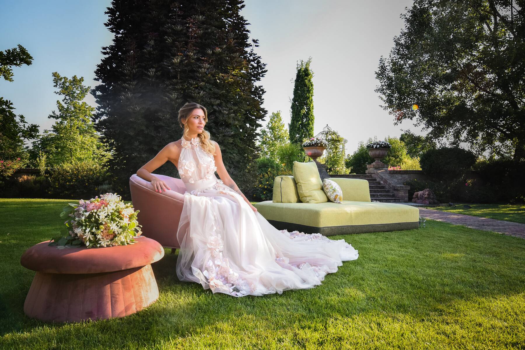Modella in abito da sposa fotografata in giardino tra i divani outdoor durante uno shooting editoriale