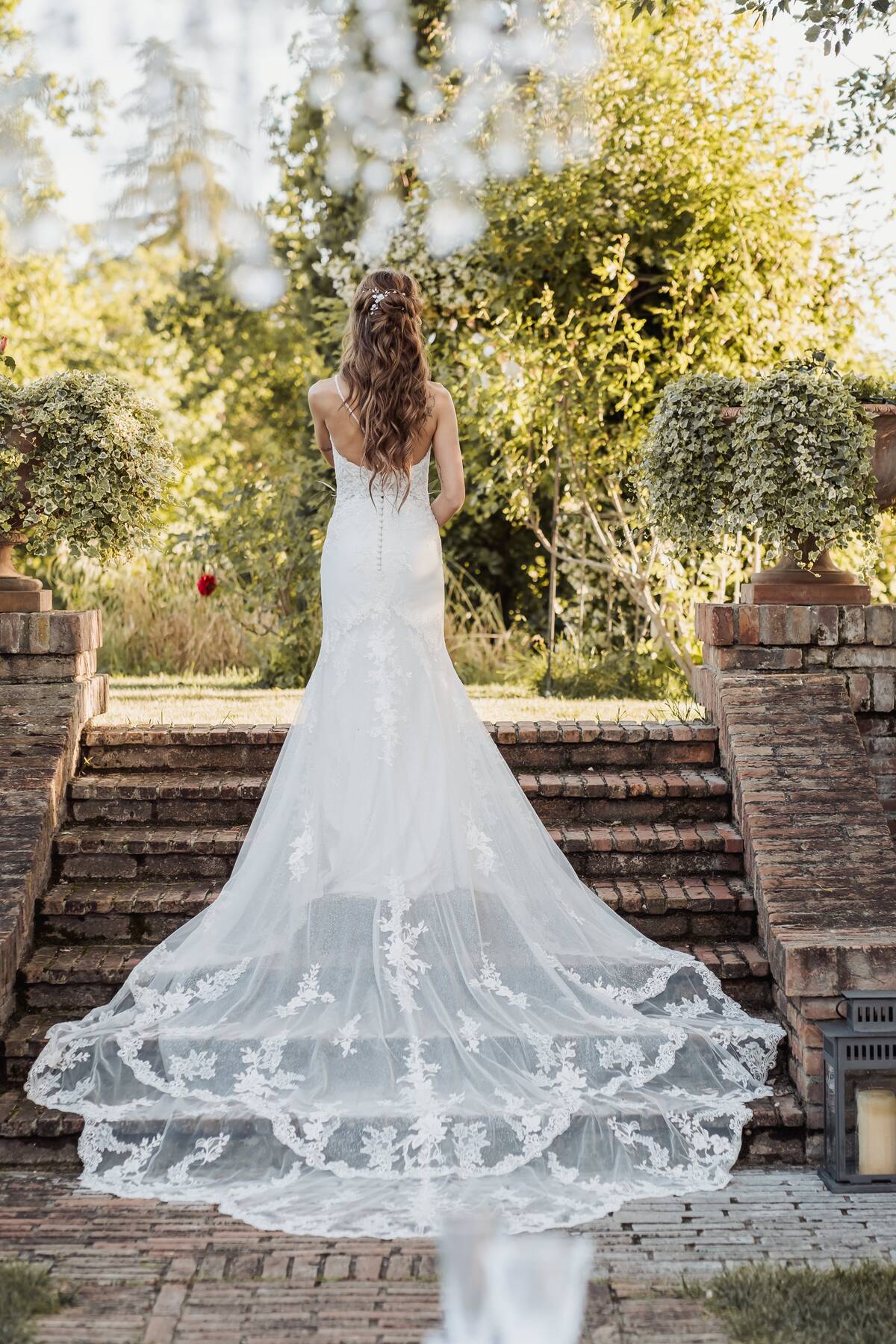 La sposa di spalle sulla scalinata del giardino, con lo strascico in pizzo
