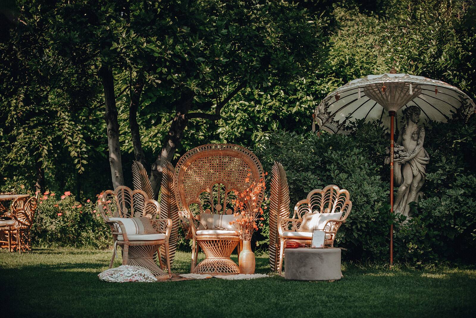 Angolo del giardino con sedie di rattan a ventaglio sul prato, ombrellone e statua