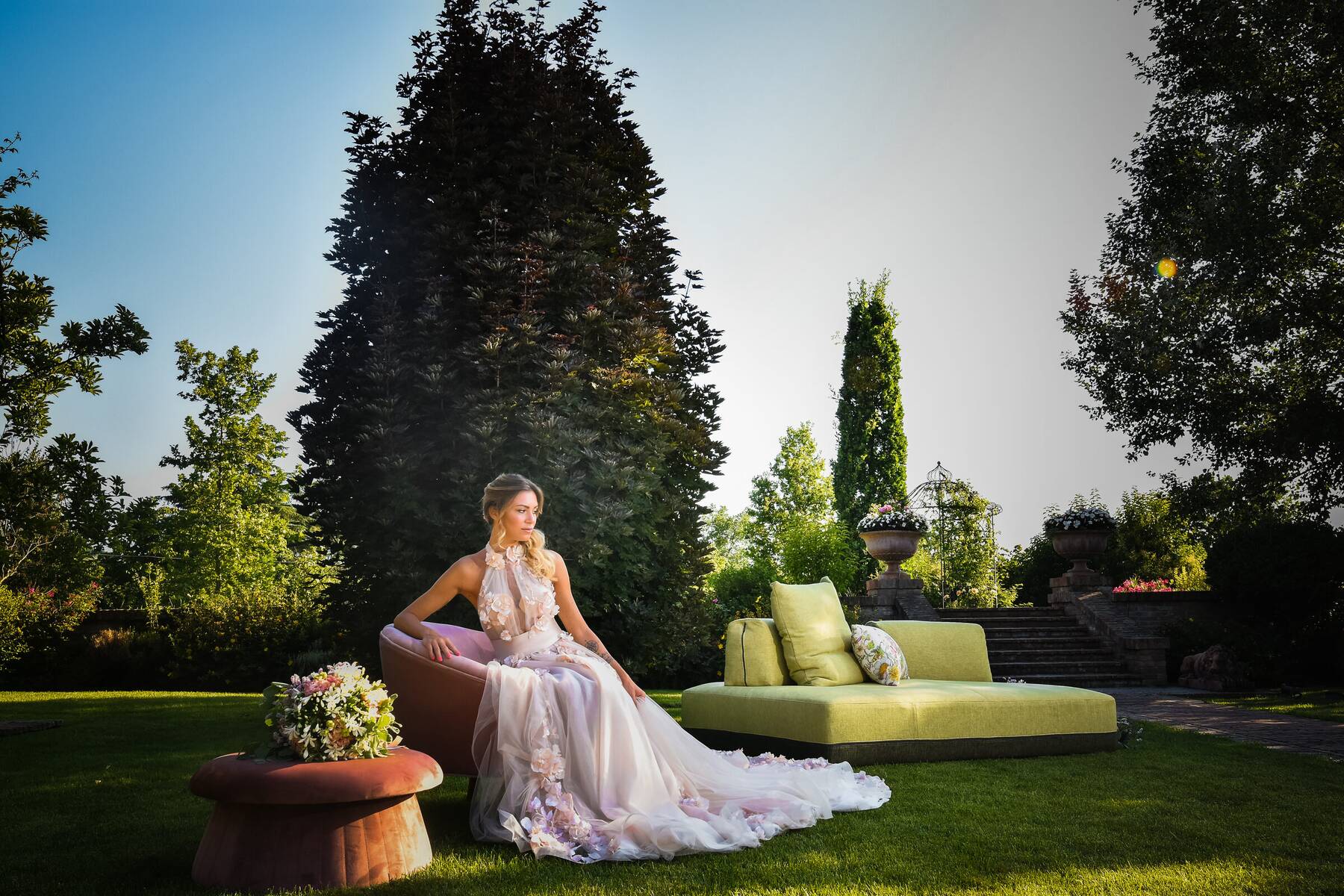 La sposa seduta nel salottino del giardino in un abito ricamato di fiori
