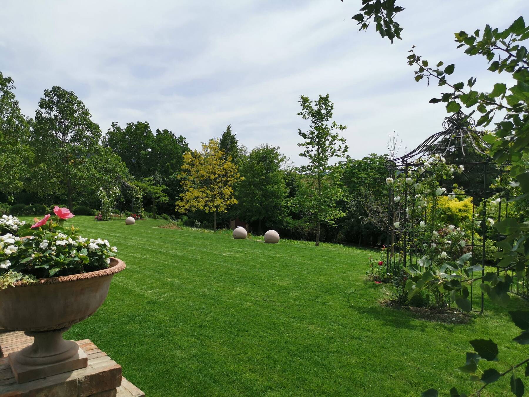 Il grande prato del Giardino delle Cerimonie con le sfere decorative in pietra e i gazebo di rose sullo sfondo