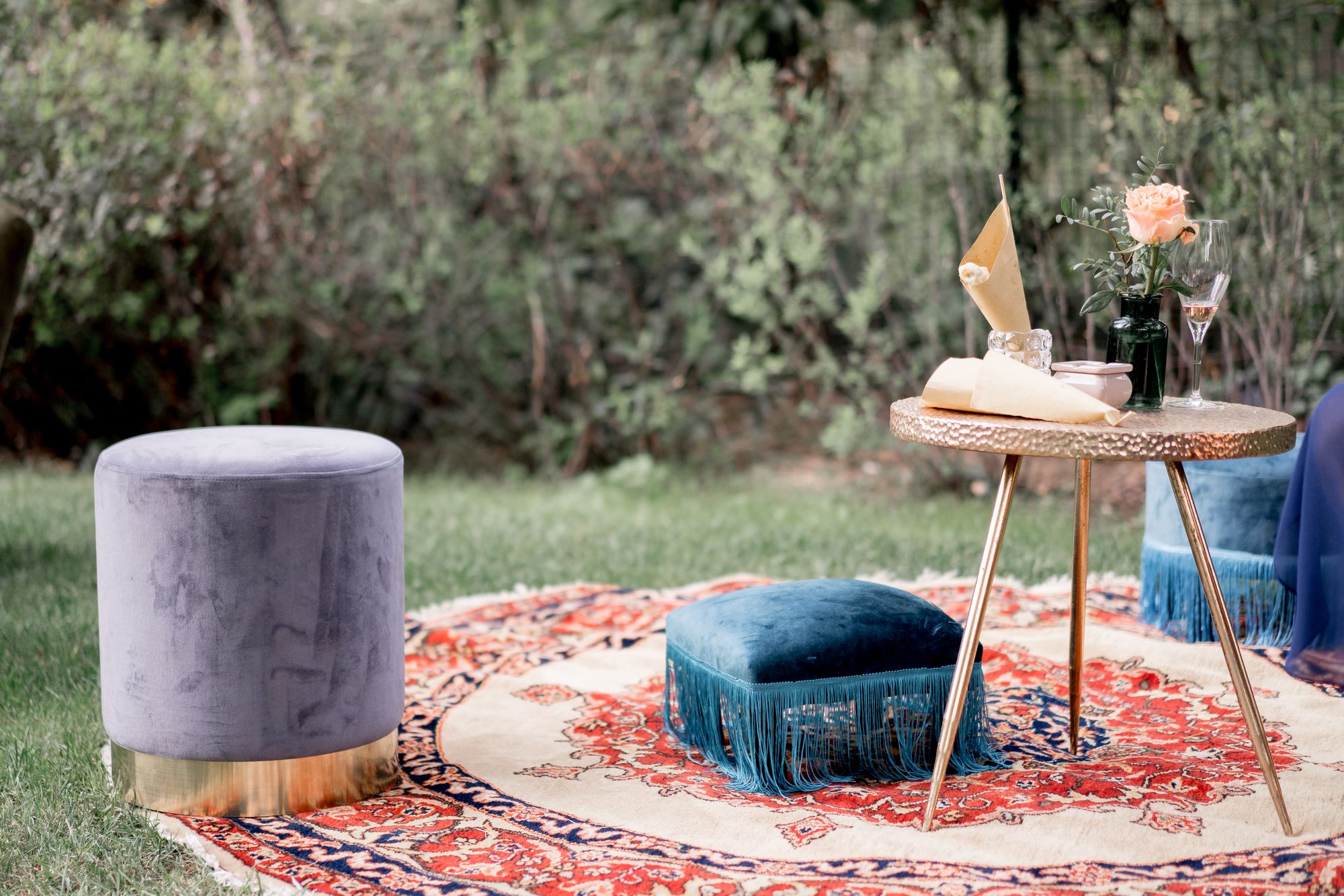 Salottino boho in giardino con pouf in velluto frangiati e tavolino in ottone martellato