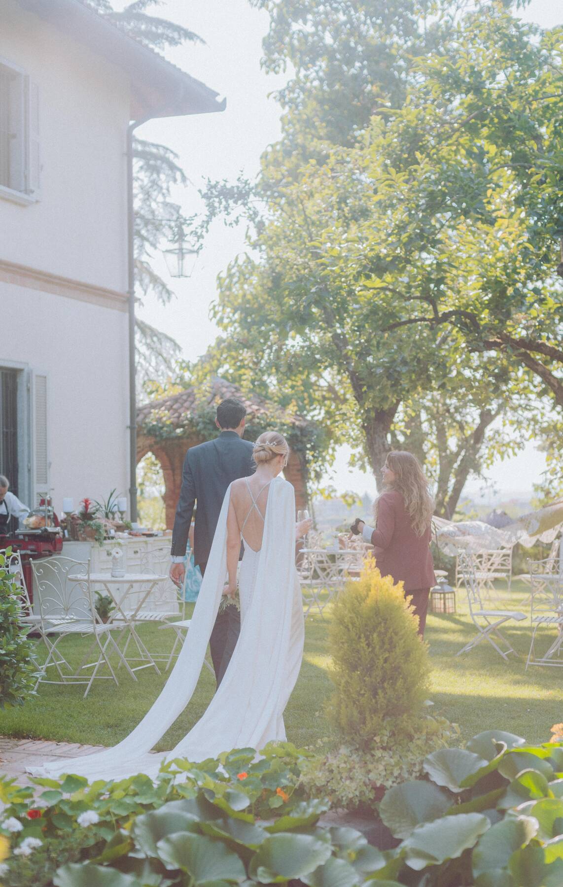 Gli sposi di spalle attraversano il giardino verso l'aperitivo