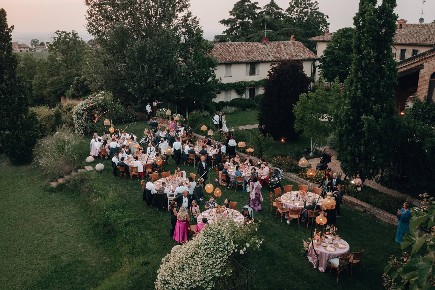 Vista dall'alto della cena in giardino con tavoli rotondi e ospiti al tramonto