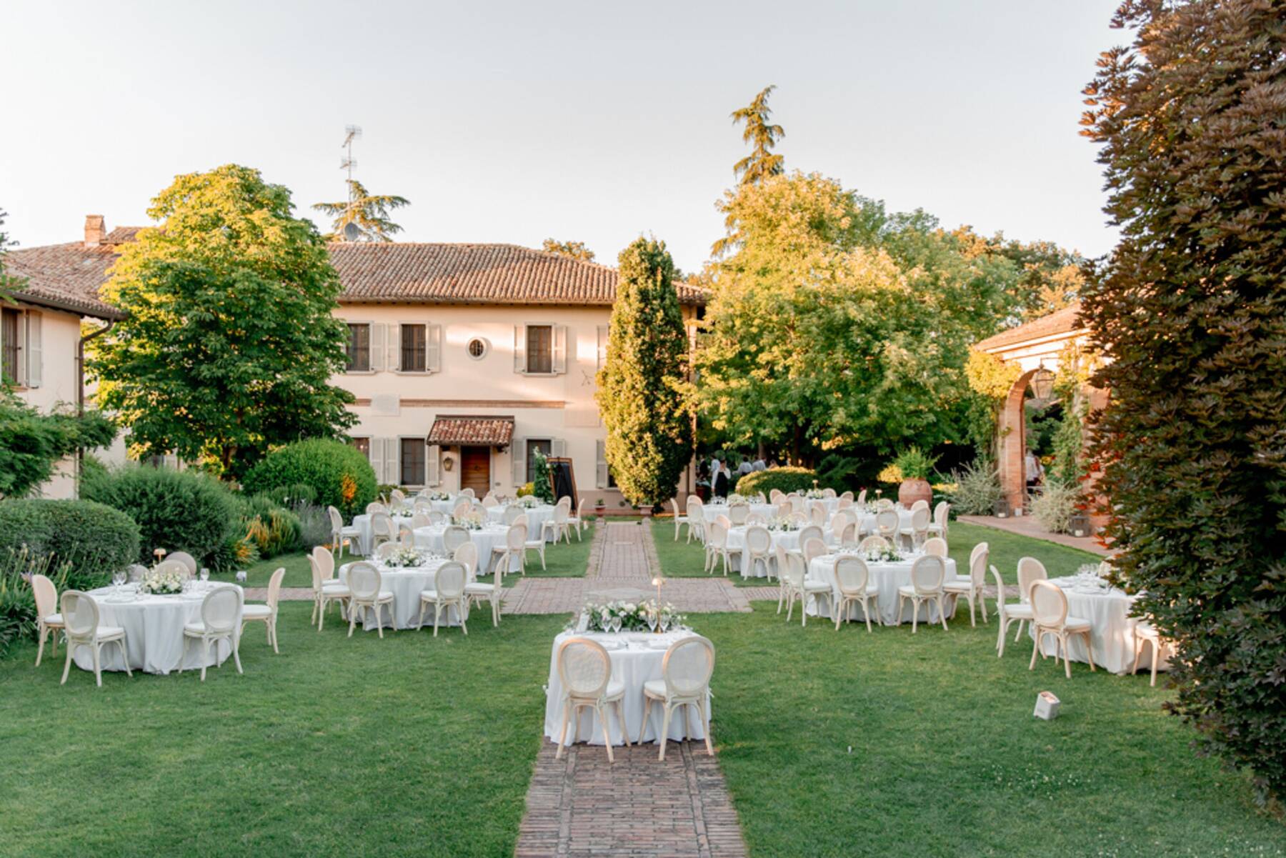 Tavoli rotondi imbanditi in giardino con sedie in rattan chiaro